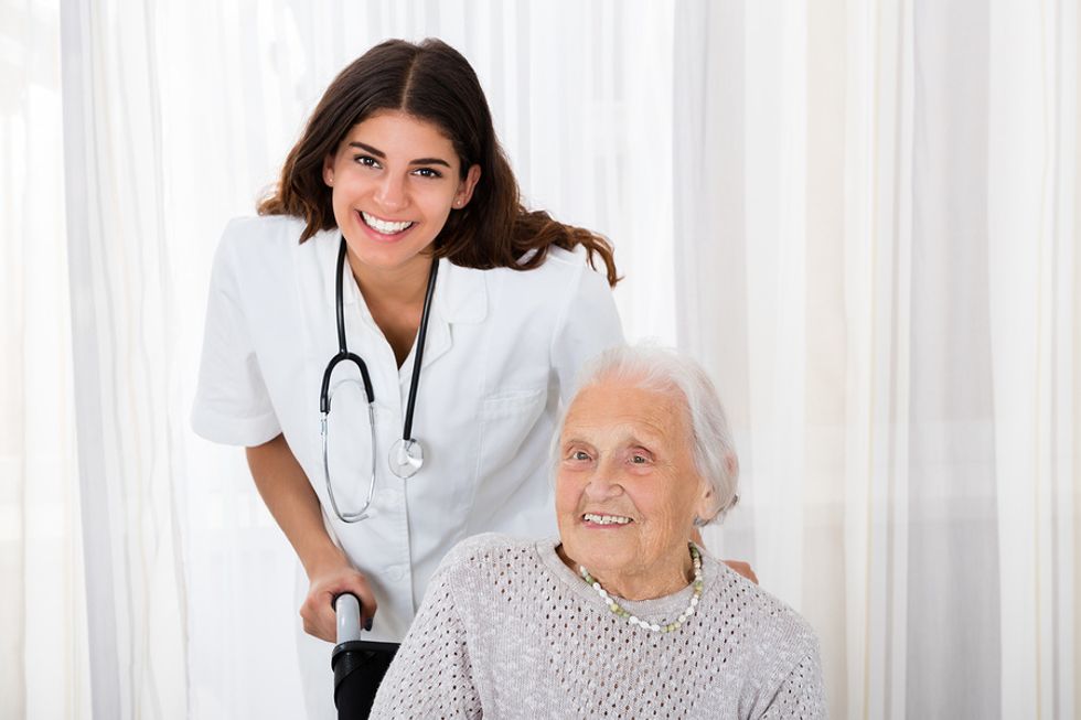 Young female traveling nurse helping an older woman in a wheelchair.