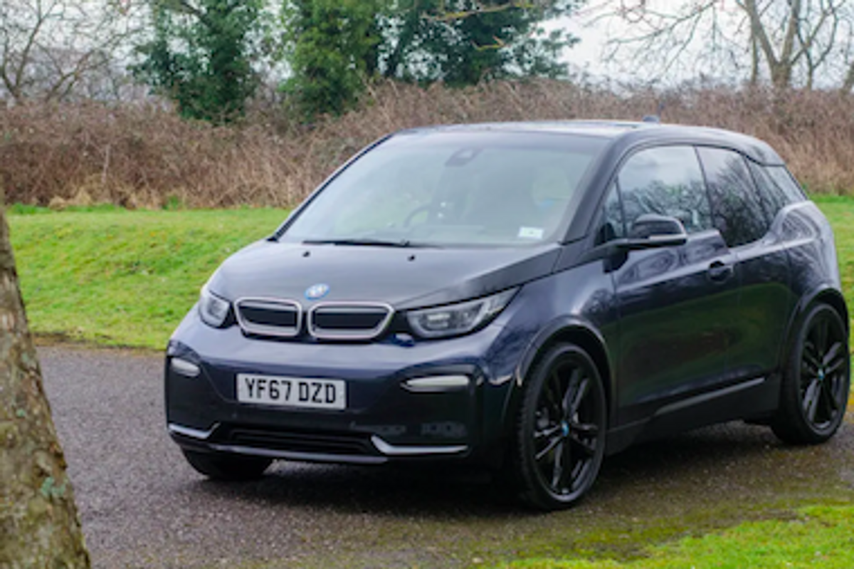 The BMW i3 electric car in black in a parking area surrounded by grass and trees