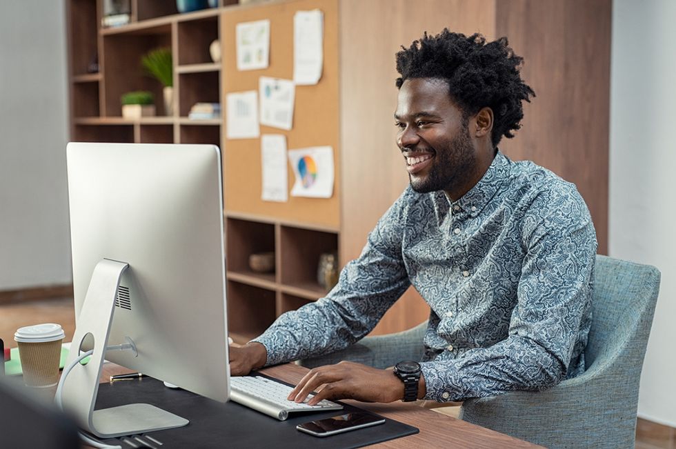 Young professional man smiling at his desk in an office, feeling happier about his work situation.