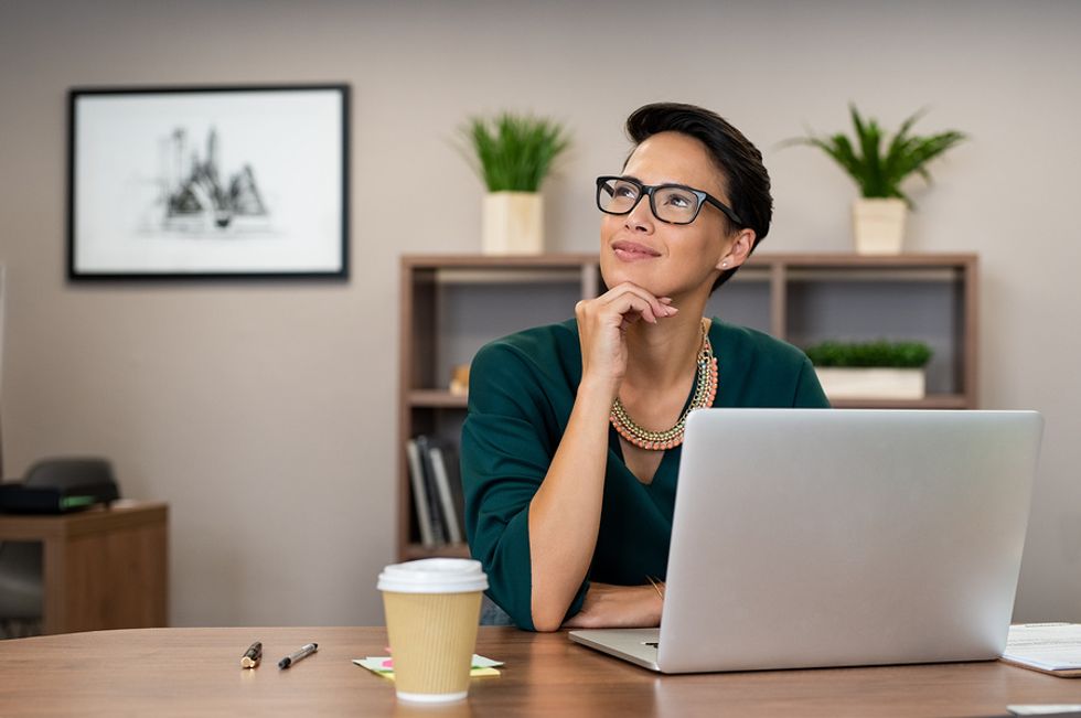 Young woman thinking positively about her work while working at her desk.