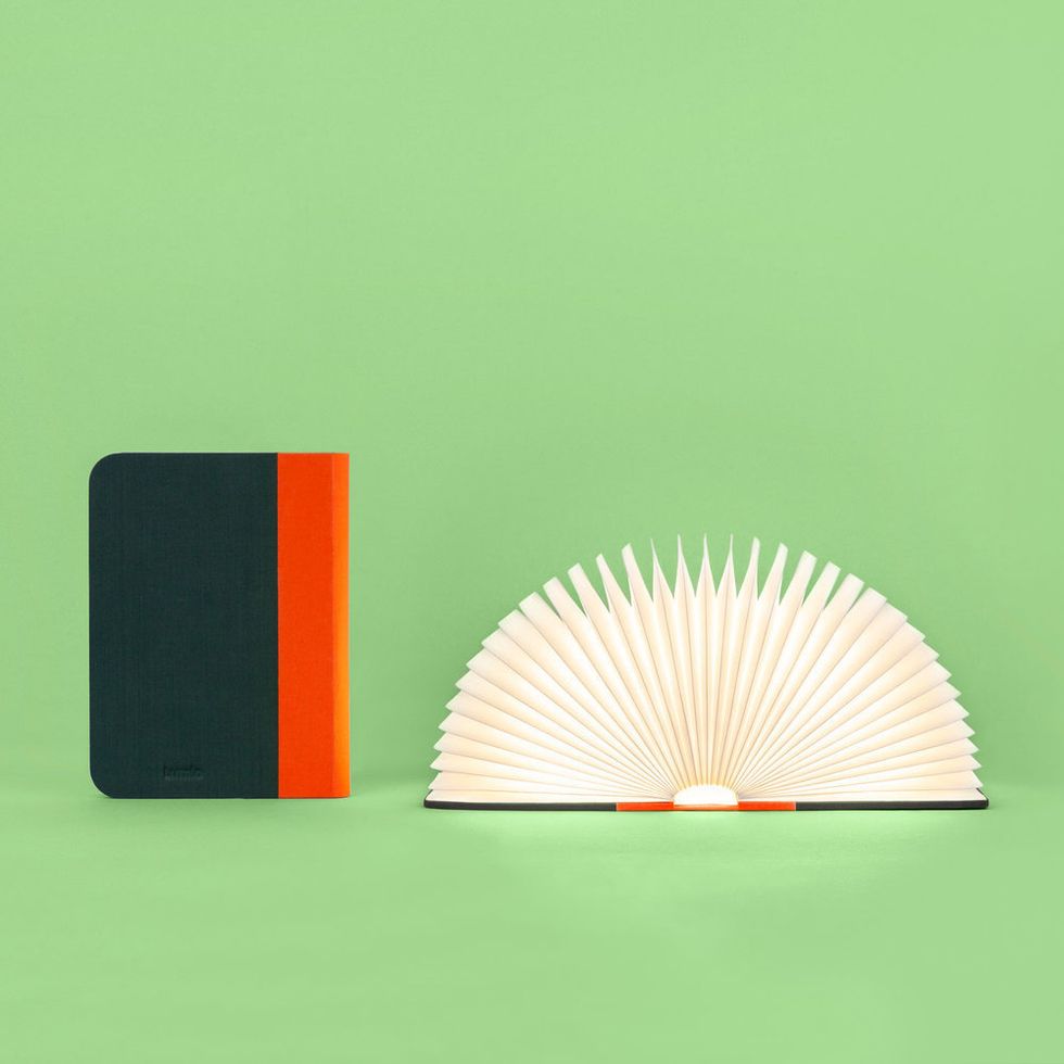 The Lumio Book Lamp in red and black against a green background