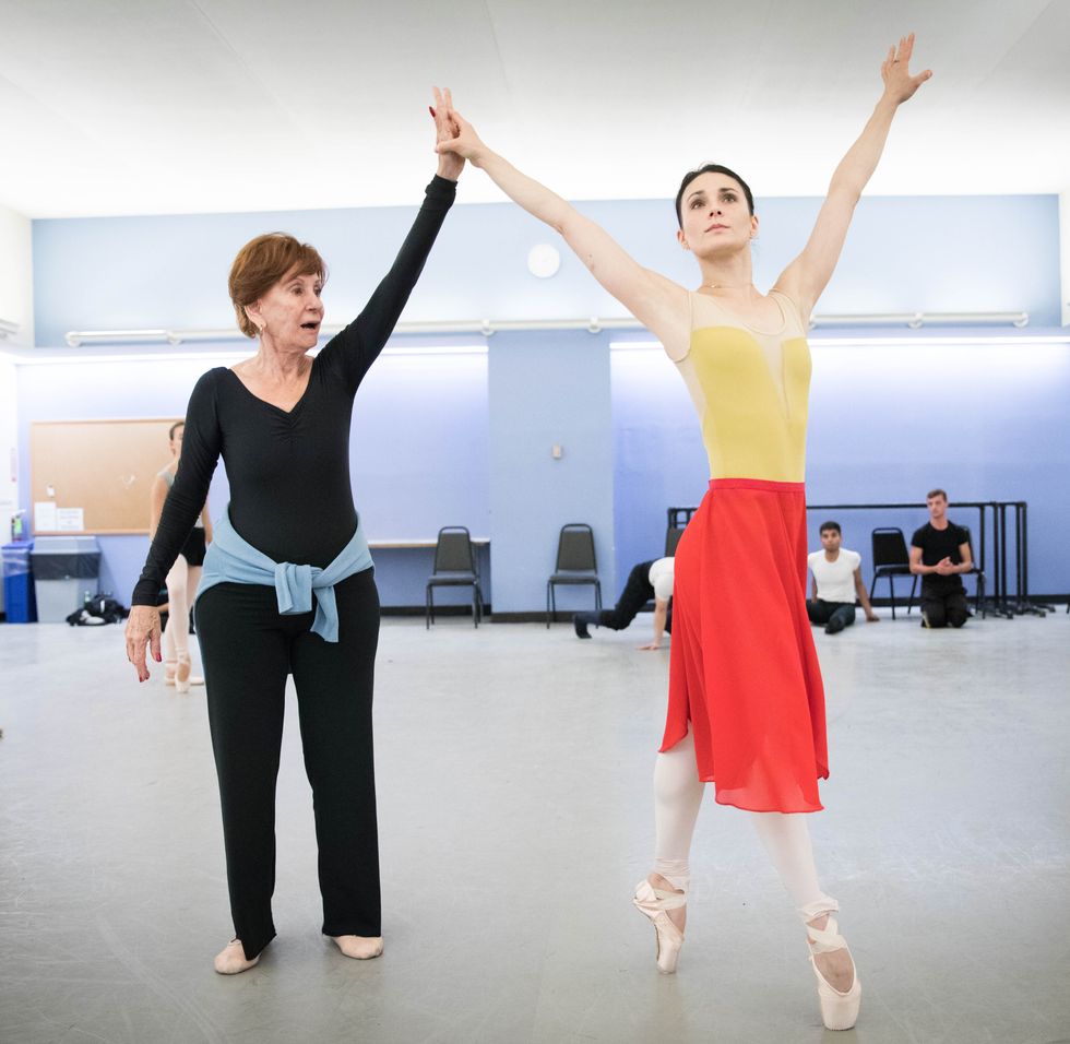 Sonia Calero-Alonso, wearing a black leotard and yoga pants, holds ballerina Sarah Lane's right hand as she balances on pointe.