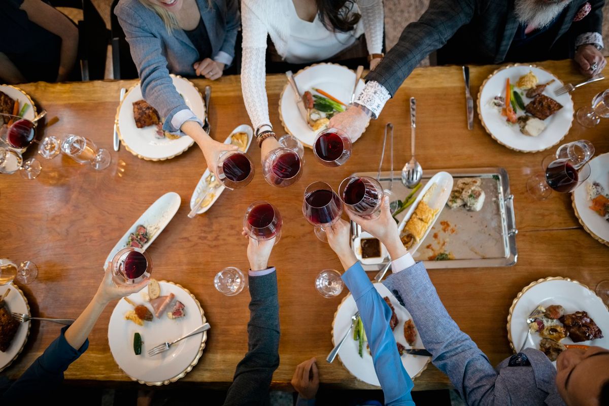 group of people cheering at a dinner table with wine glasses 