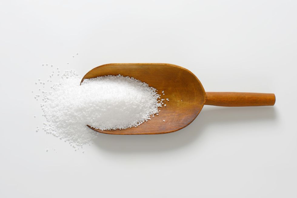 Salt spills out of a wooden spoon on a white background