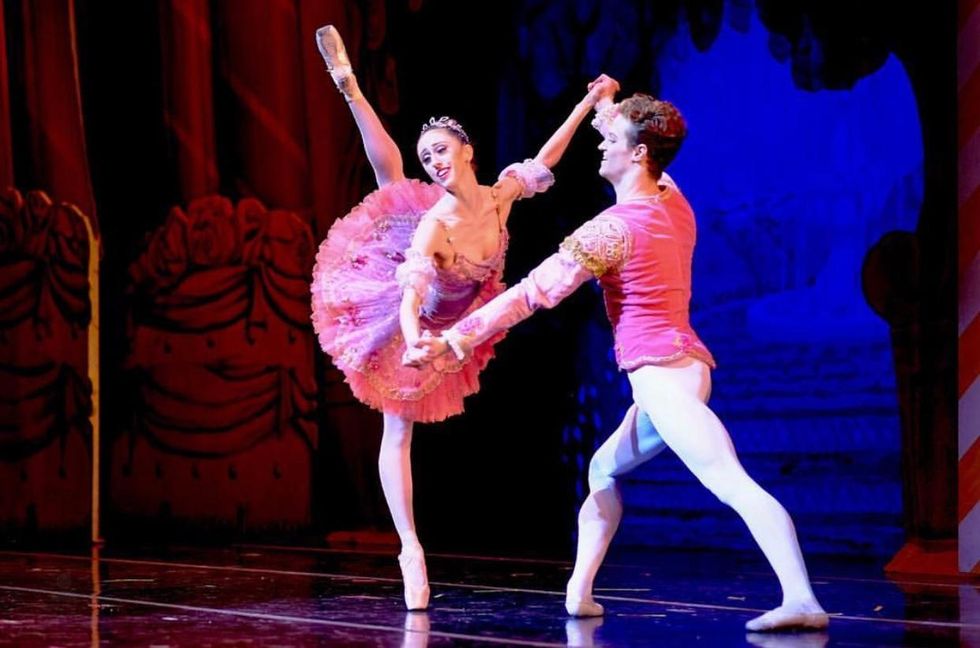 Sam Ainely, in a pink tunic and white tights, partners a ballerina in a purple tutu on pointe.