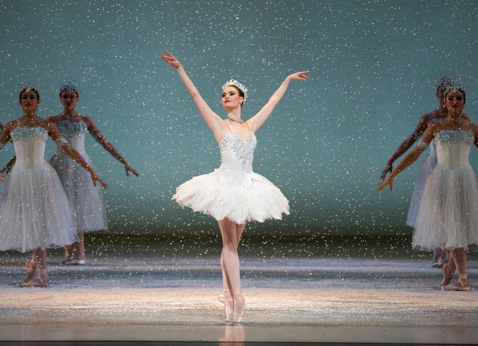 Elizabeth stands onstage with her feet together in sus-sous on pointe. She wears a white tutu and crown, and there is fake snow falling around her.