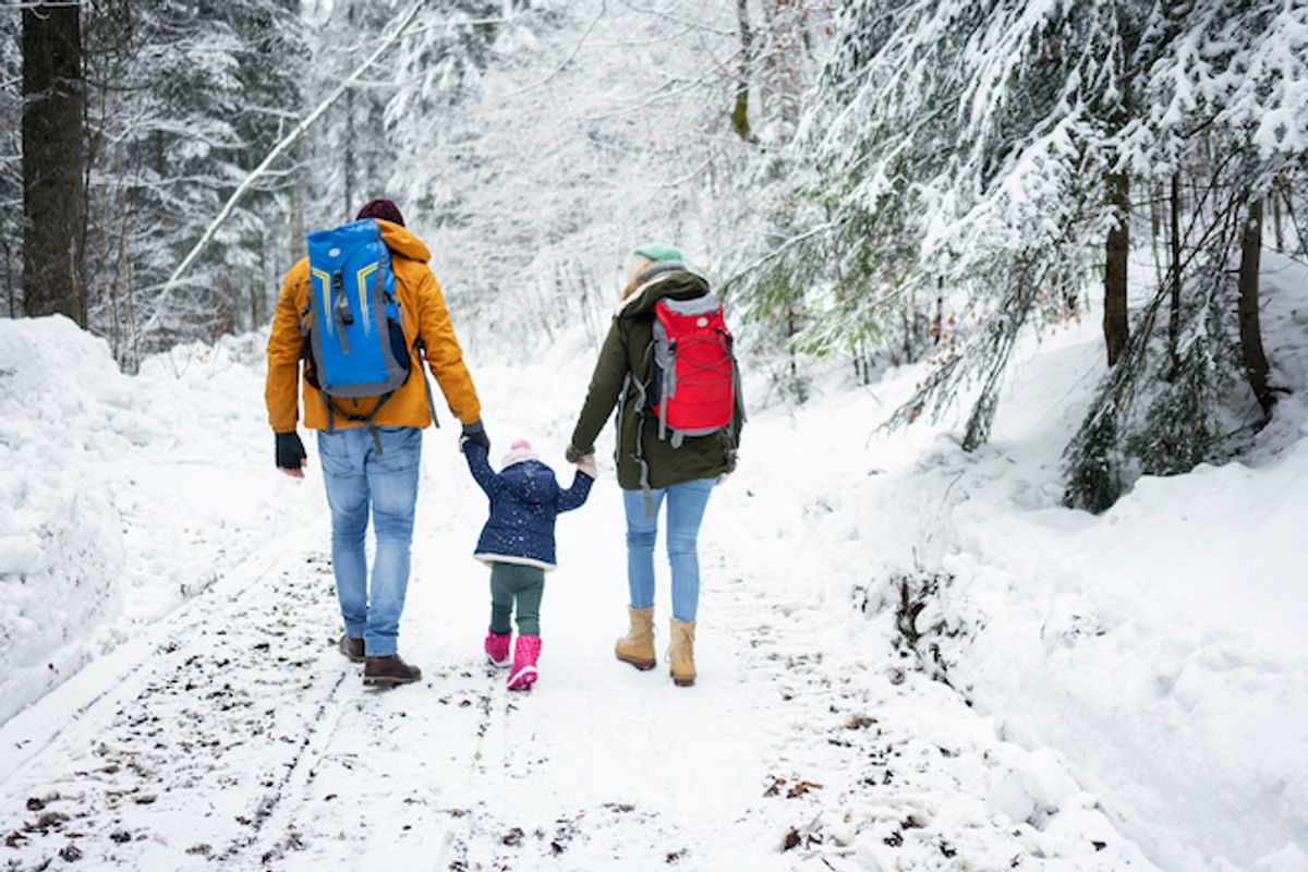 A family with a child holding hands while walking in nature, outdoors in the snow