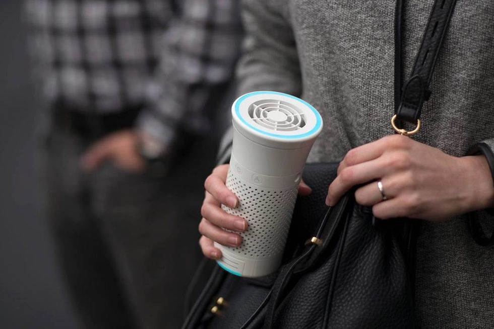 Someone holding a Wynd Plus air purifier while wearing a black bag