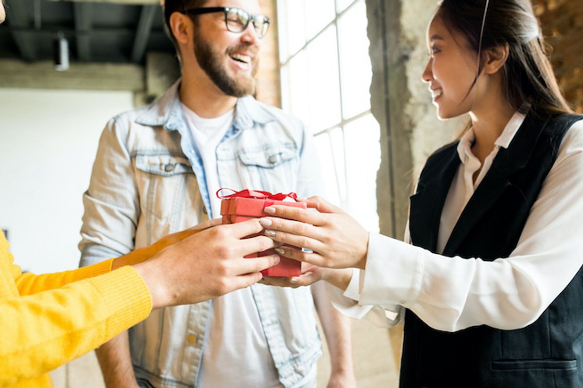 Three people exchanging gifts in an office space with a large window