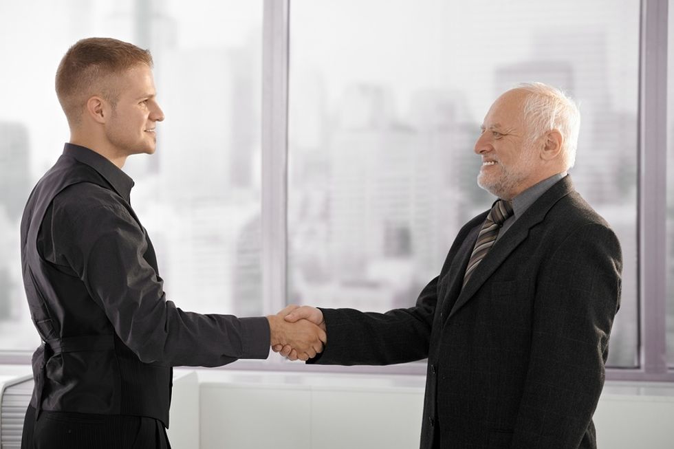 Young professional man shaking hands and networking with an older executive man in an office.