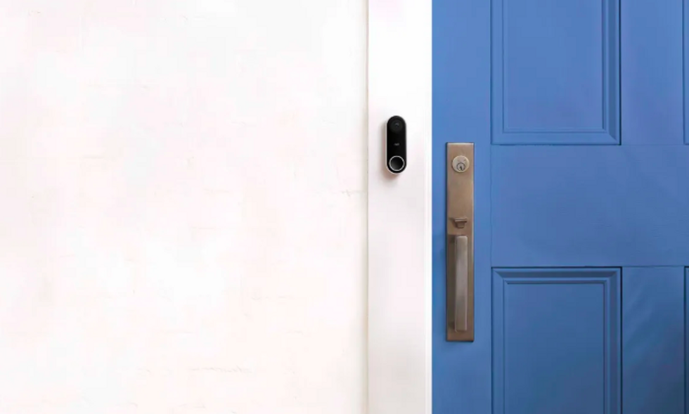 A Nest Hello video doorbell on a white wall next to a blue door