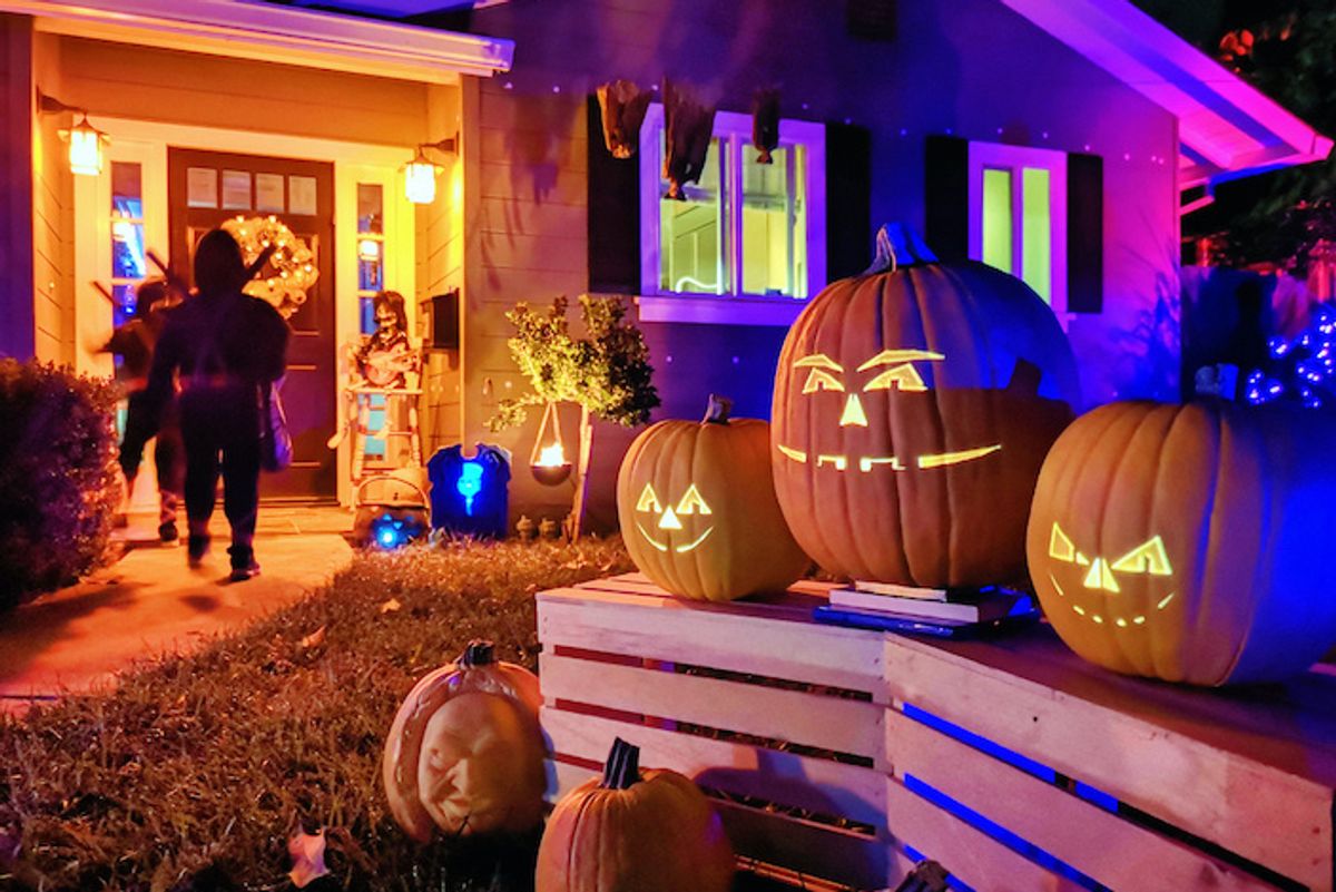 People walking to a front door bathed in orange light, with carved pumpkins lining the way