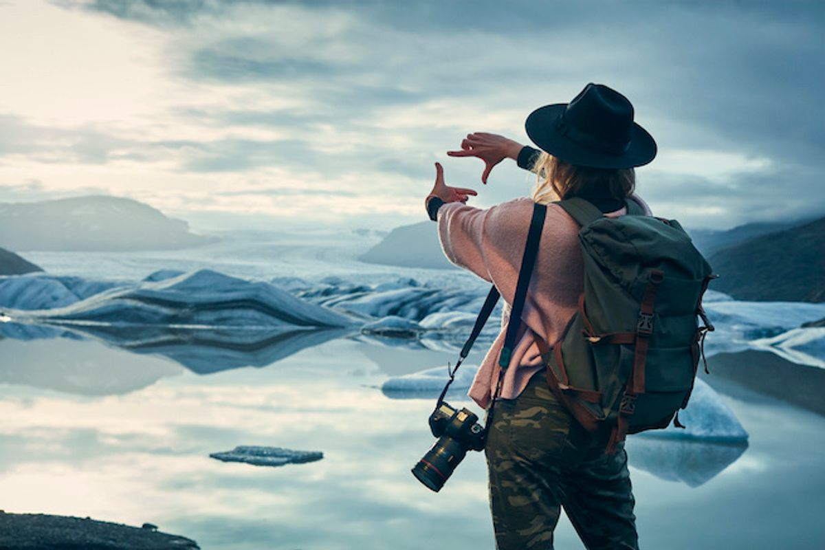 A traveler standing in front of a glacier, wearing a backpack and camera