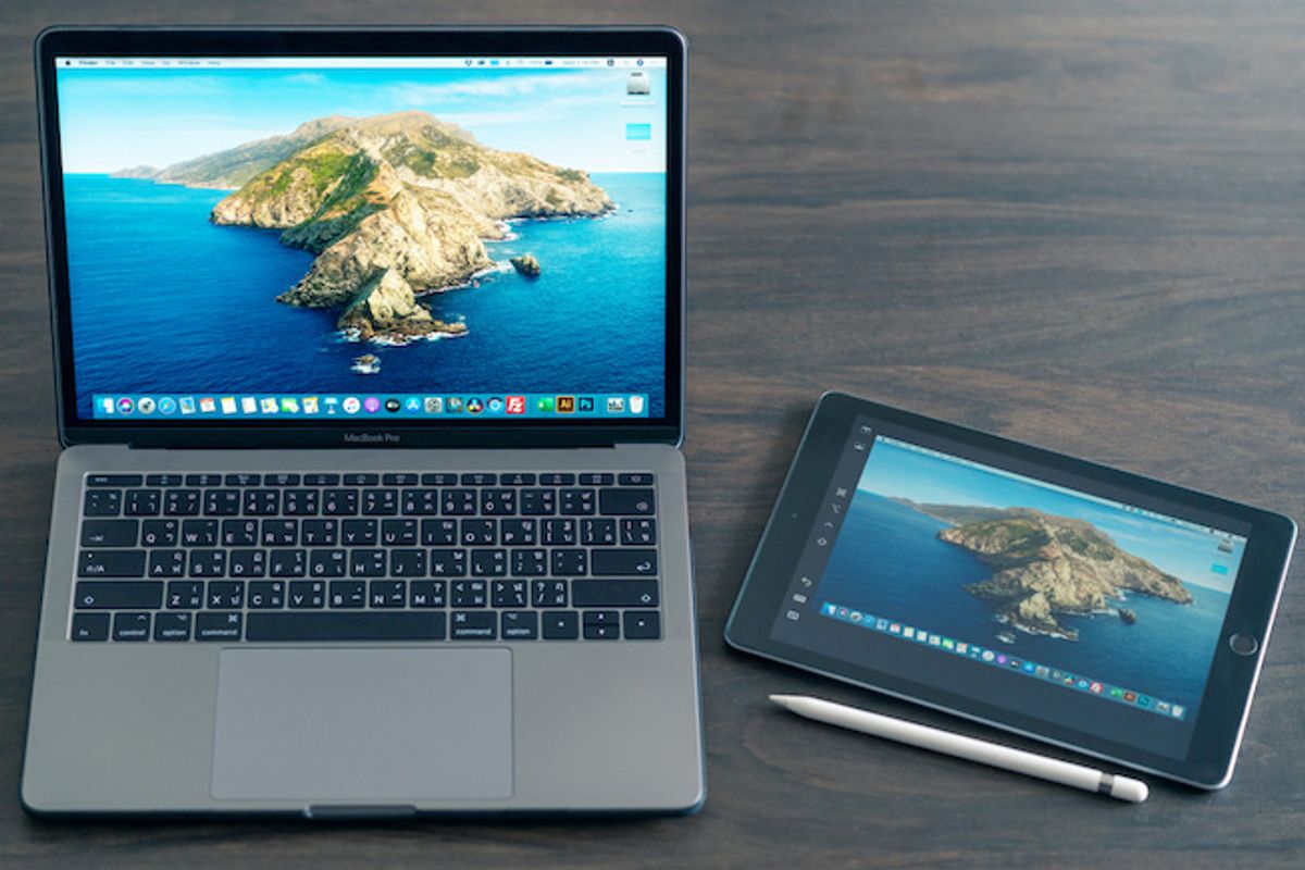 An Apple MacBook Pro and an iPad side by side with an Apple pen, on a wooden table