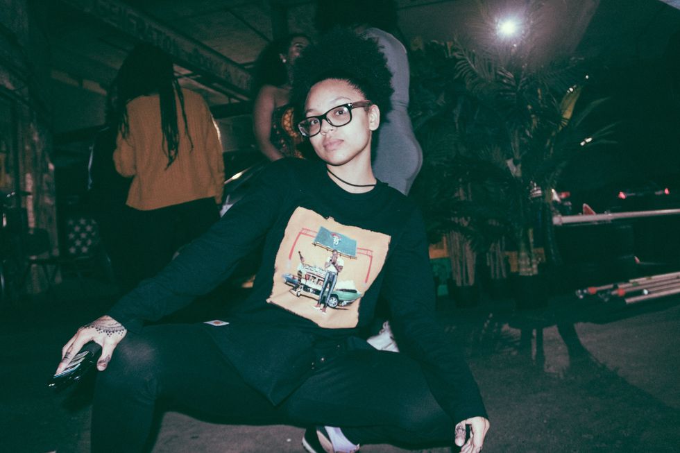 Model wears Jidenna's "85 to Africa" longsleeve T-shirt backstage while doing a rap squat.