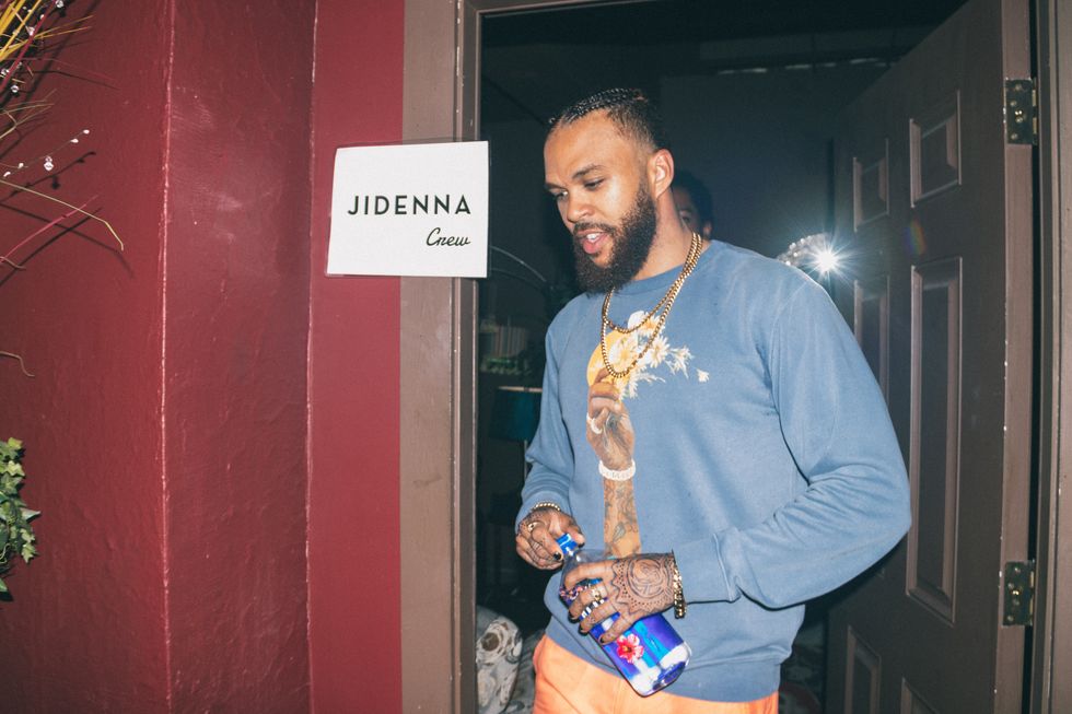 Jidenna stepping out of his dressing room in a stylish blue sweater.