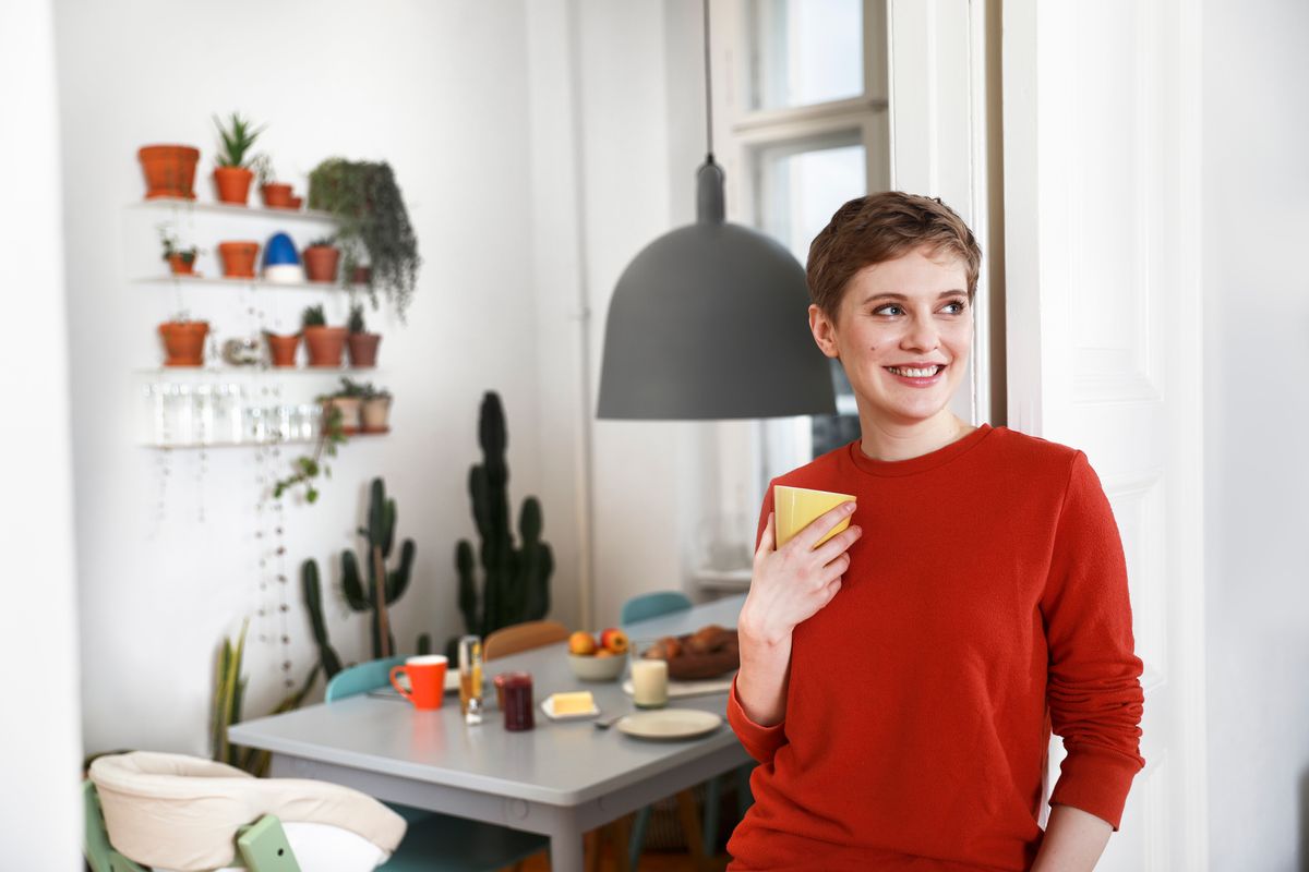 Woman standing in her kitchen smiling holding a mug