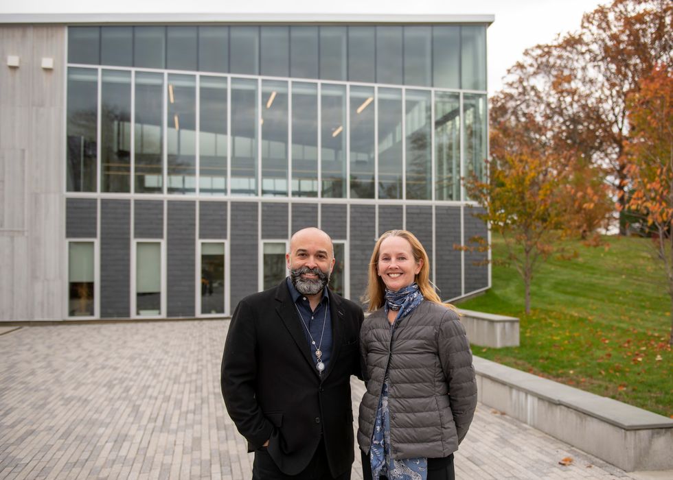 Antonio Vivo and Margaret Tracey, wearing jackets, pose standing next to each other outside a school building.