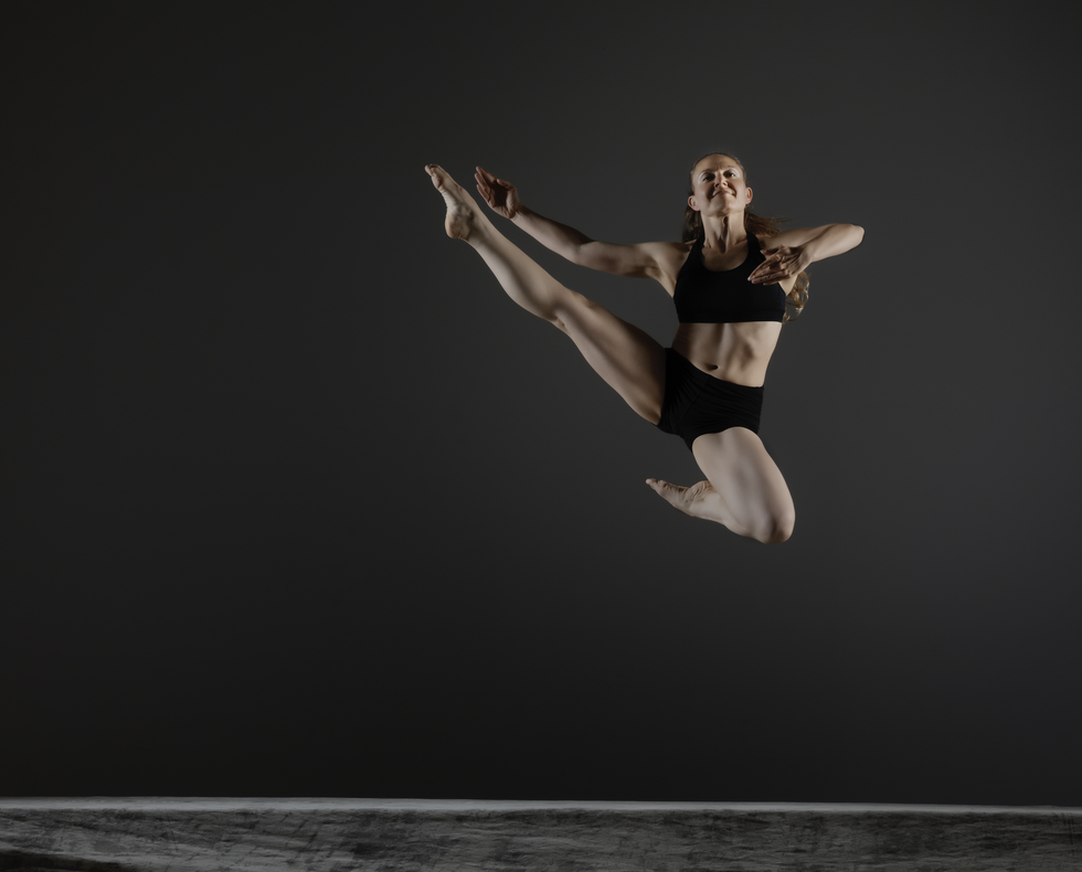Zahna Simon leaps high off the stage, on leg in developpe side, the other tucked tightly underneath her.