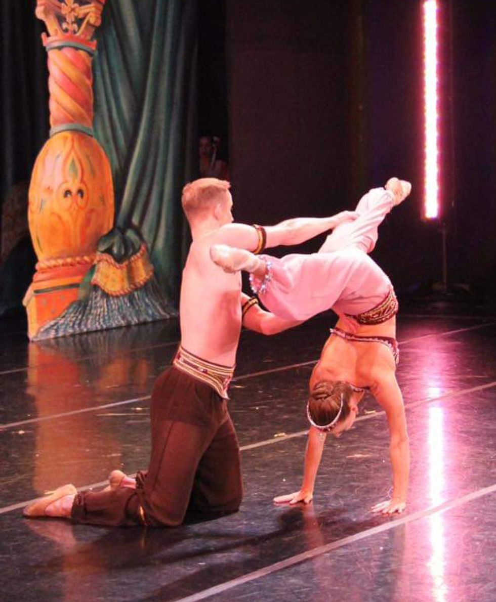 Luke Joiner helps Jennifer Goodman with a back walkover onstage during a Nutcracker performance. They both wear harem pants, and Goodman wears a sparkly top.