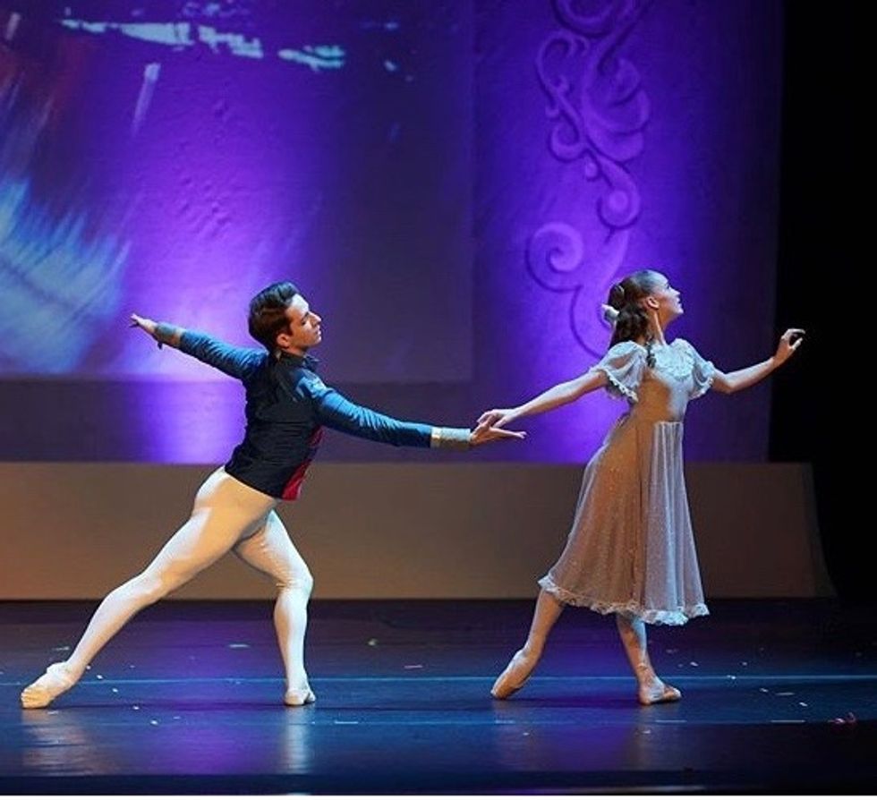 Michael Breeden, in a blue jacket and white tights, reaches for his partner's right hand during a performance.