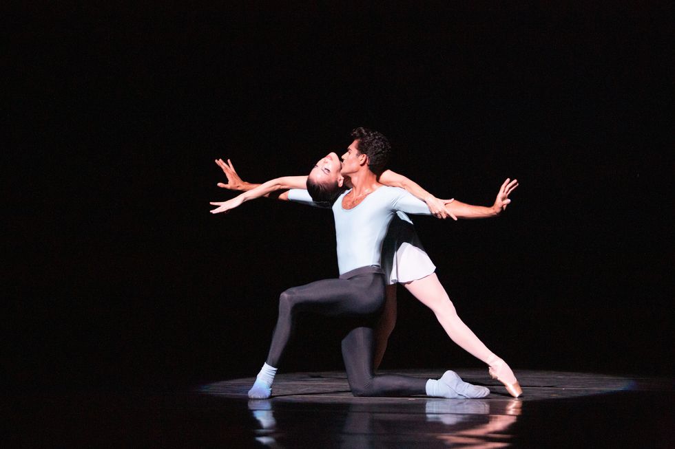 Renan Cerdeiro, in black tights and a blue shirt, knees on his right knee with arms outstretched as Katia Carranza bends backwards over them.