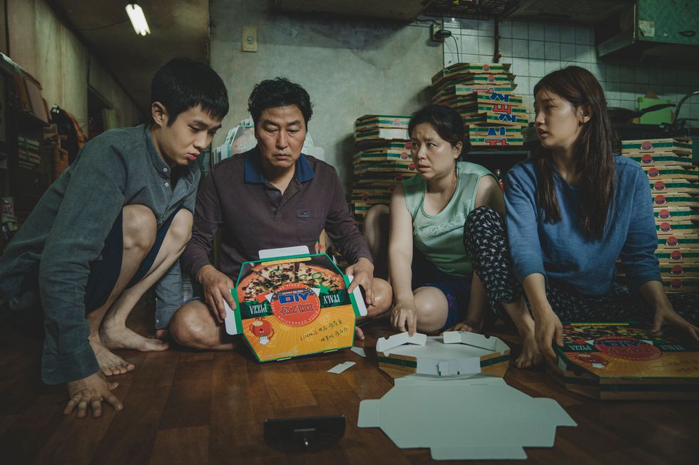 The Kim Family (Woo-sik Choi, Kang-ho Song, Hye-jin Jang, So-dam Park) are surrounded by folded pizza boxes as they sit on the floor of their cramped, poorer apartment in "Parasite."