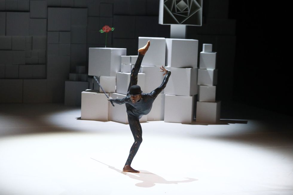 Stanley Glover, standing center stage in a shiny black unitard and bowler hat, kicks his right leg all the way to his ear.