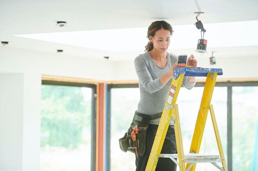 Electrician with smartphone installing a device in the ceiling in a home