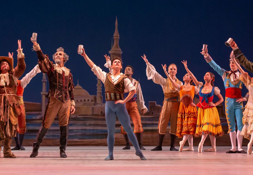 Francisco Estevez, in blue tights and a brown vest, holds a silver cup over his head along with the rest of the cast of Colorado Ballet's Don Quixote.