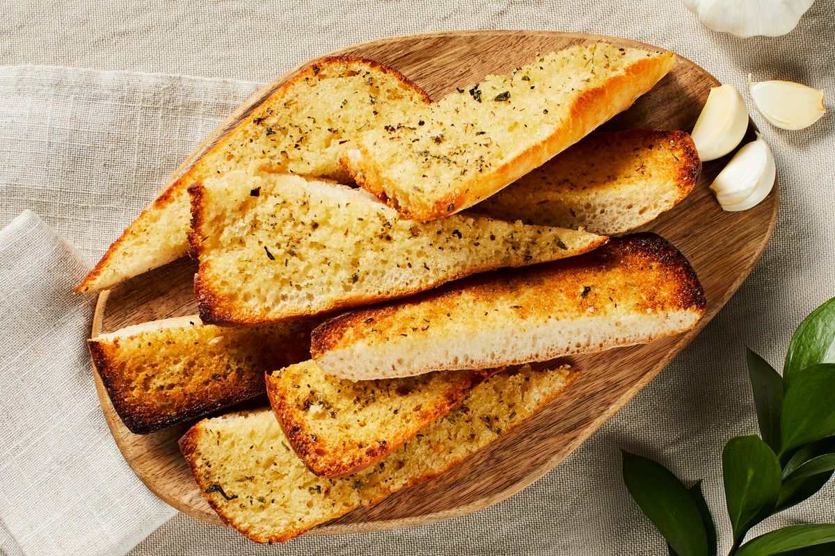 beautiful garlic bread in a wooden basket on a beige cloth with garlic cloves and a plant