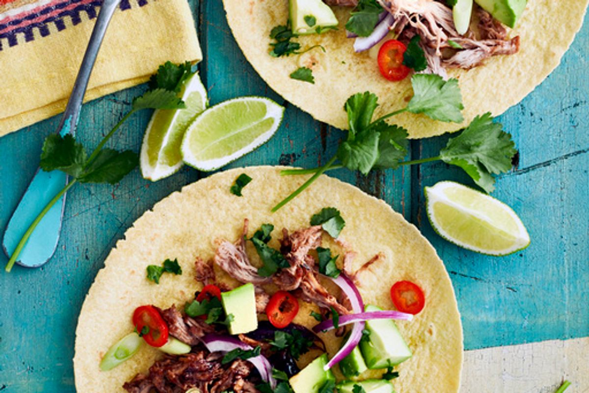 2 open-faced tacos with meats, red onion, tomato and lime on a blue table