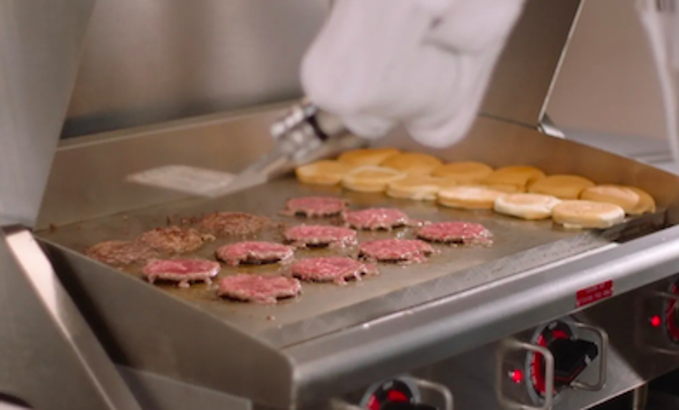 A one-armed robot flips hamburgers on a grill