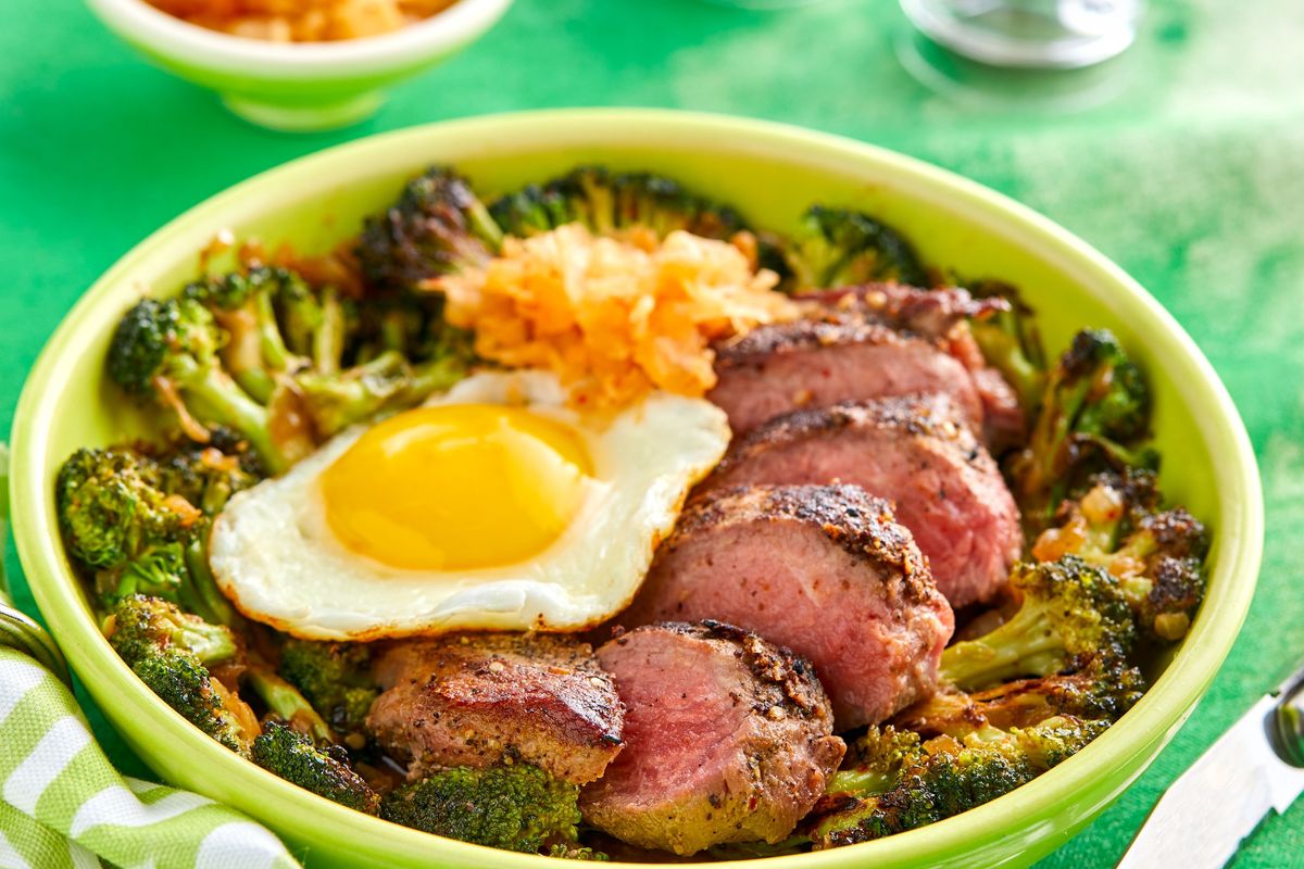 a green bowl with meat, broccoli and a fried egg