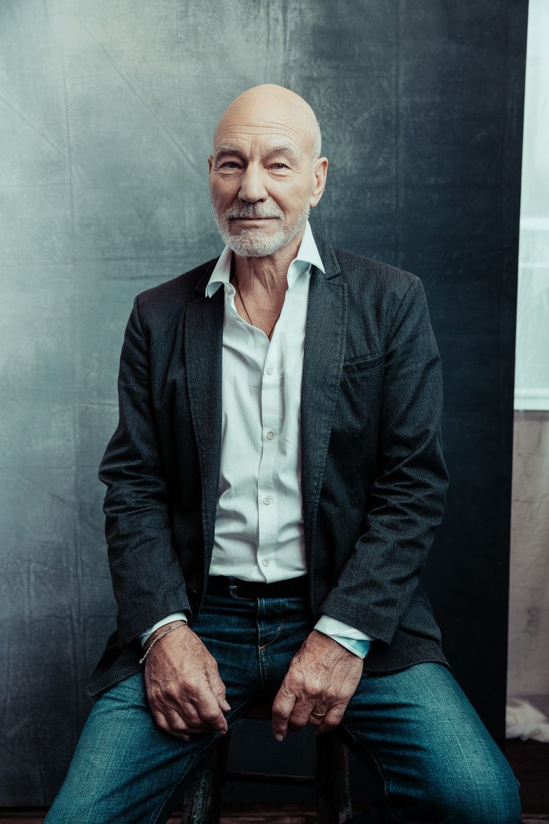 Sir Patrick Stewart sitting on a stool and smiling for a portrait.