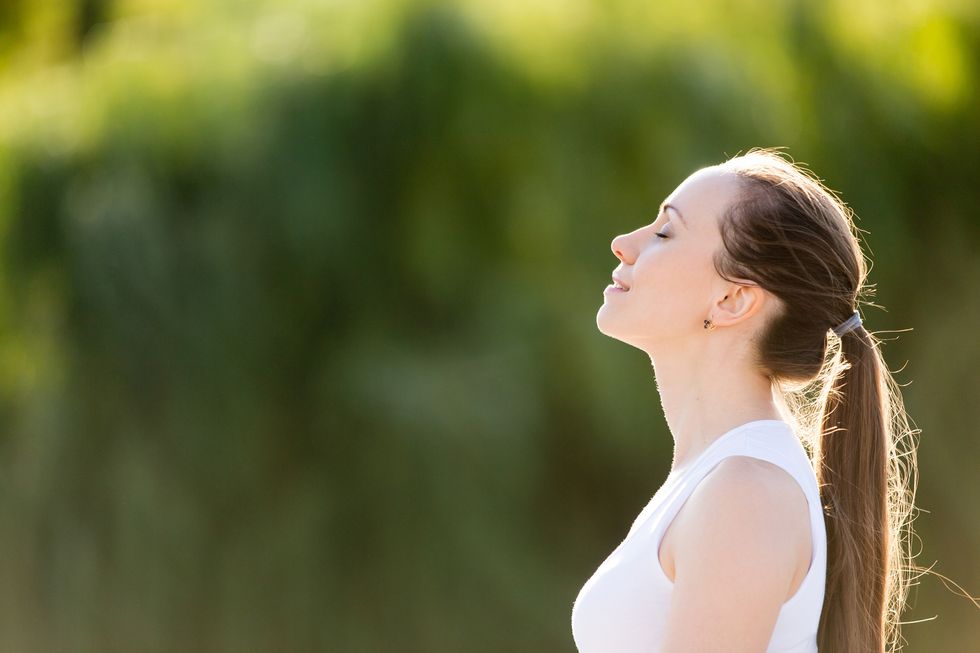 A woman sits outdoors and takes a deep breath