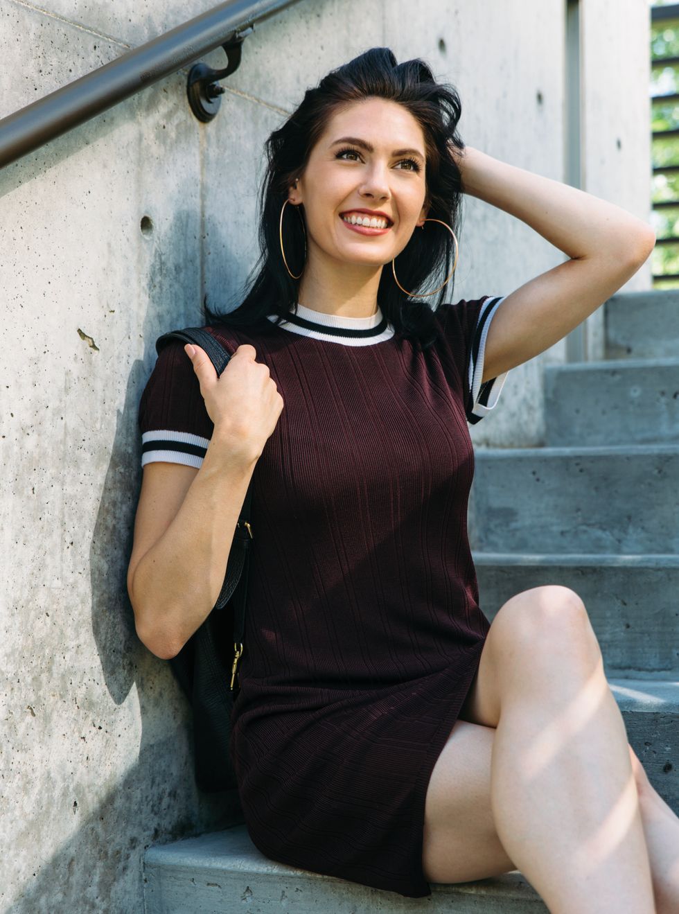 Sisk, sitting on concrete steps, pushes her hair behind her while smiling widely.
