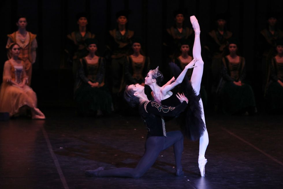 Husheng, dressed in a princely velvet jackets and black tights, supports Bingxue in an over extended pench\u00e9. She's wearing a black Odile tutu and crown.