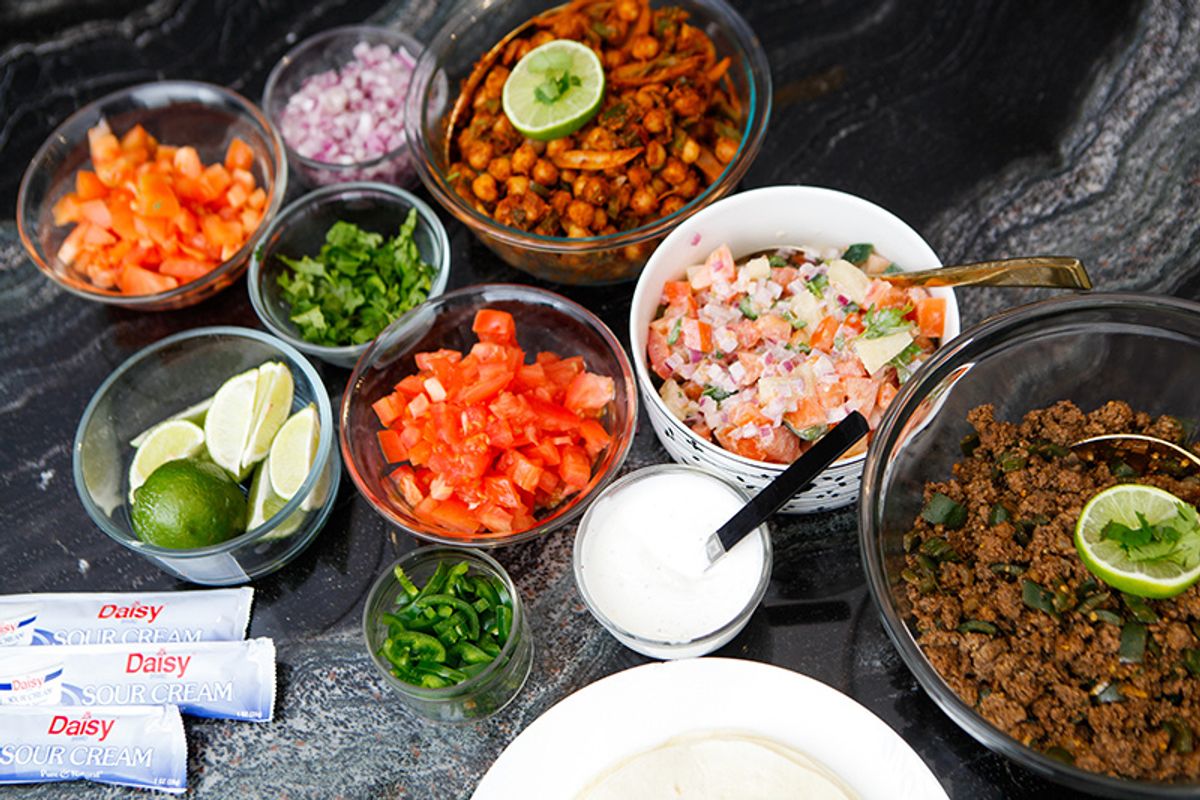 Brightly colored taco ingredients in bowls - tomatoes, chickpeas, beef, limes, jalapenos, onions and cilantro