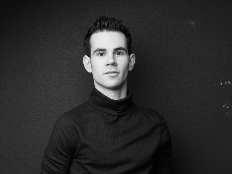 Victor Prigent is shown from the elbows up in a black and white portrait, looking directly at the camera with a small closed smile. HE has short dark hair, dark eyes and wears a black turleneck shirt.