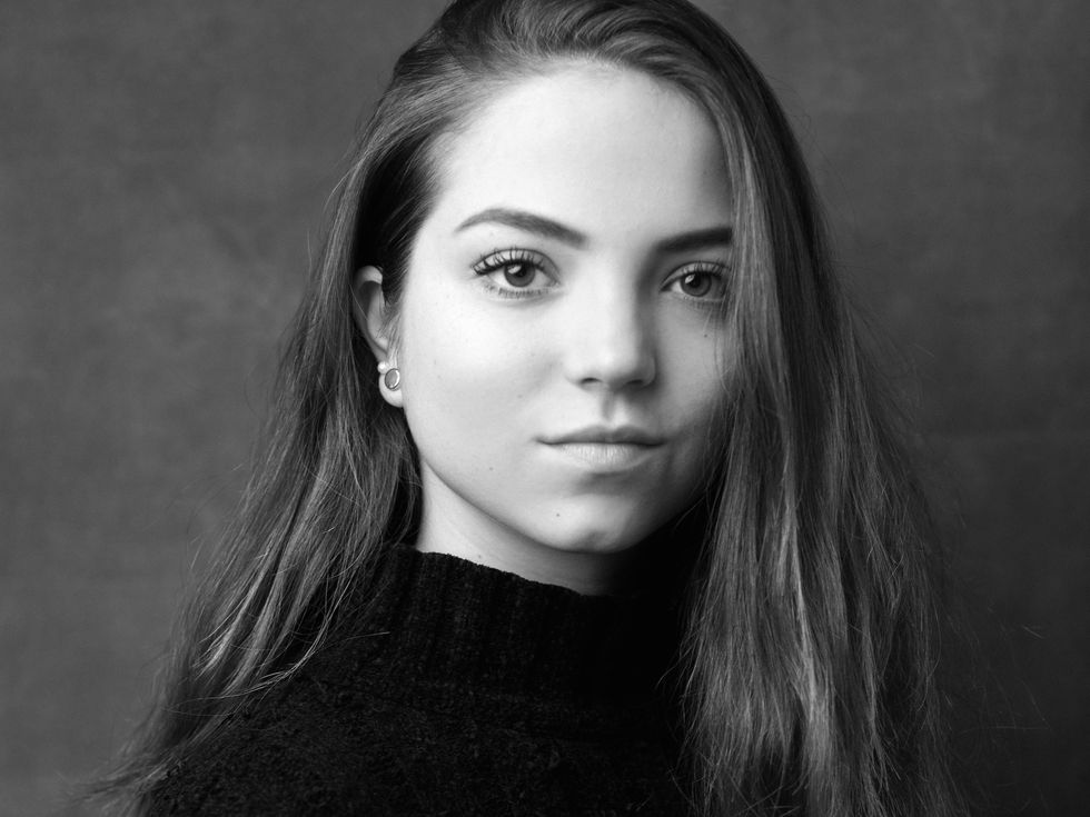 Ivana Bueno is shown from the shoulders up in a black and white portrait, looking directly at the camera with a small closed smile. She has long light brown hair and wears a dark turtleneck sweater.