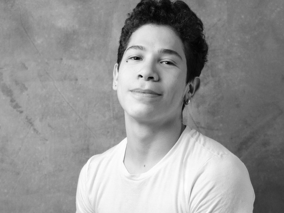 Miguel Angel Maidana is shown from the shoulders up in a black and white portrait, looking directly at the camera with a small closed smile. He has short, curly hair, brown eyes and wears a white T-shirt and a small hoop earring in his left ear.