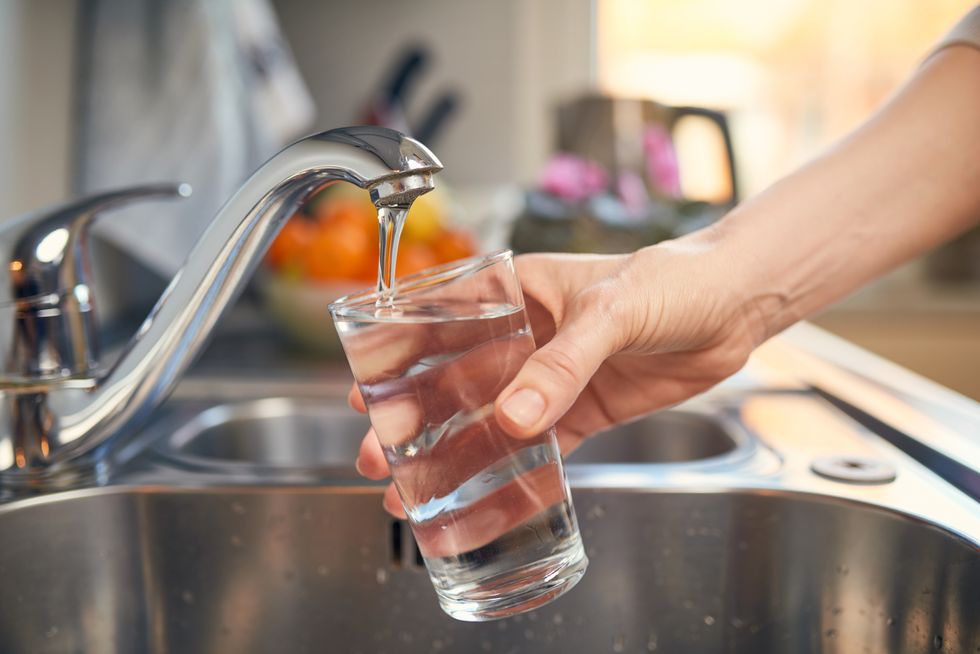 A hand fills a glass of water at a metal sink.
