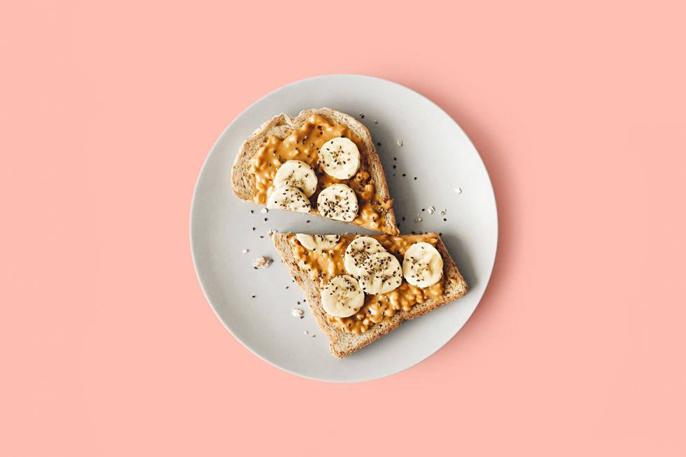 Bananas and peanut butter and chia seeds on toast on a white plate against a pink background.