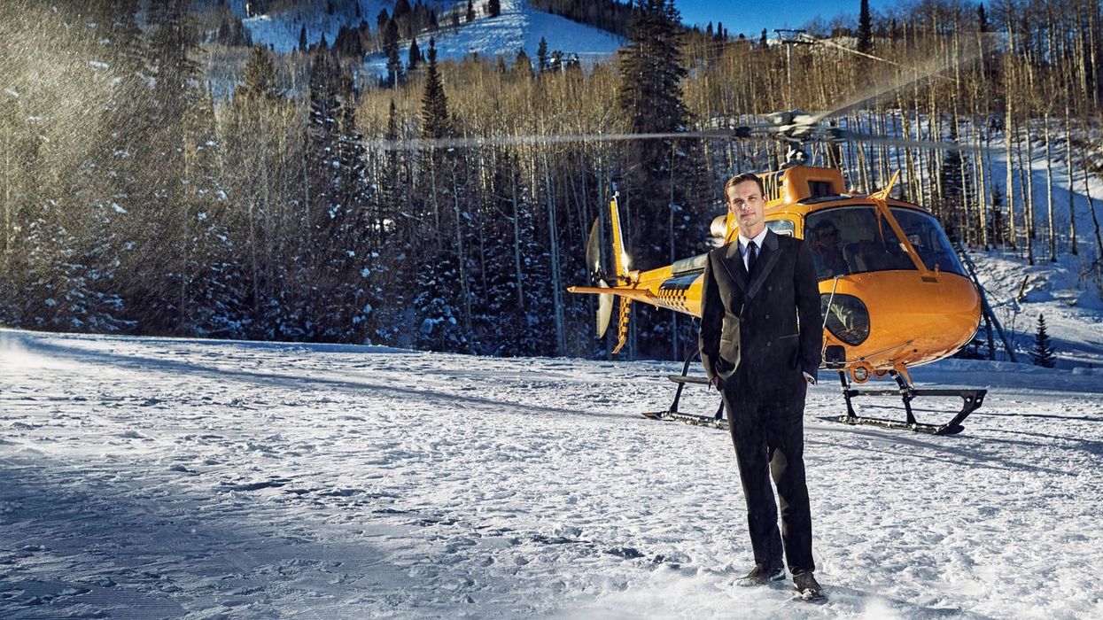 Matthew Gray Gubler in a black tux in the snow in front of helicopter.