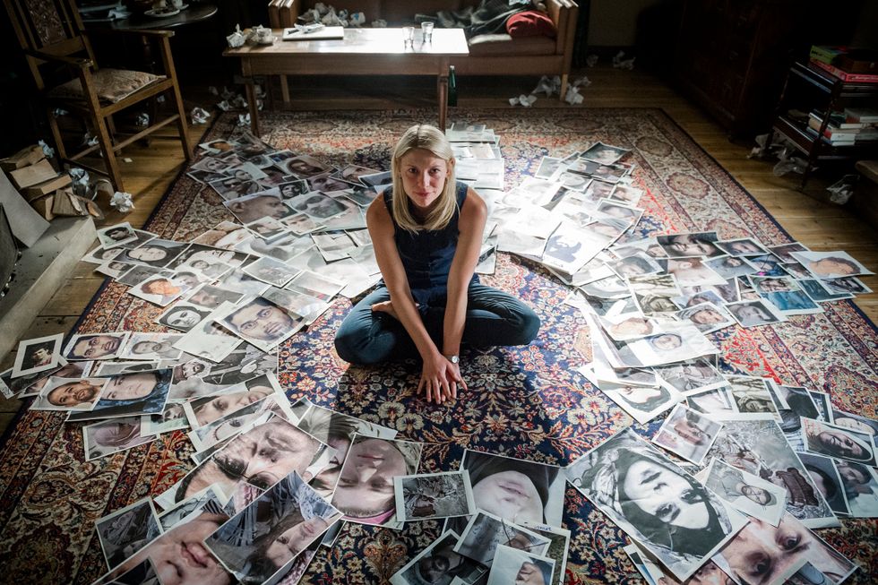 Claire Danes sitting on a pile of photographs.