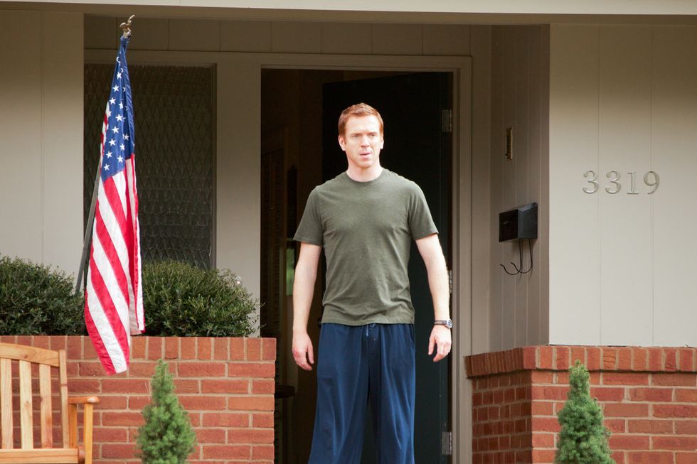 Damian Lewis standing outside home flying the American flag.