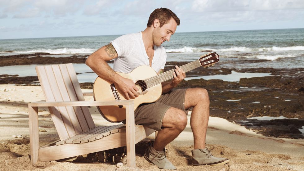 Alex O'Loughlin playing the guitar on the beach.
