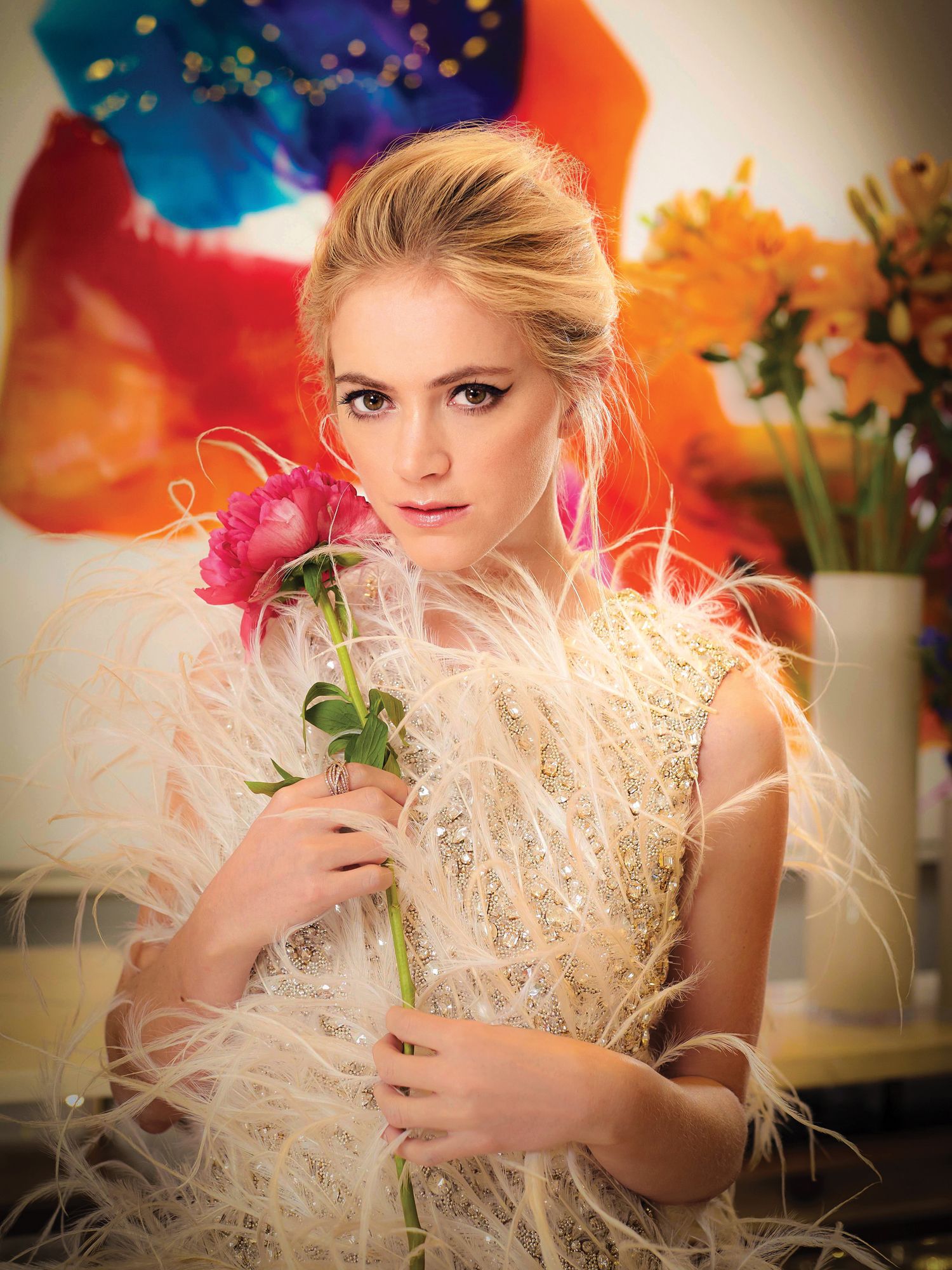 Emily Wickersham holding a pink rose and wearing a feathered designer gown