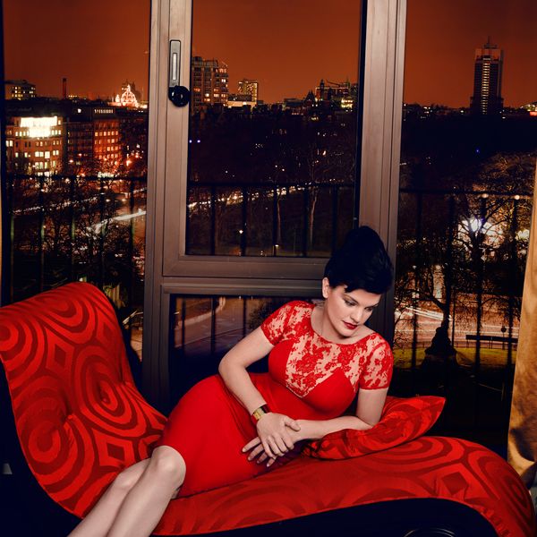 Pauley Perrette in a red dress sitting on a red sofa.